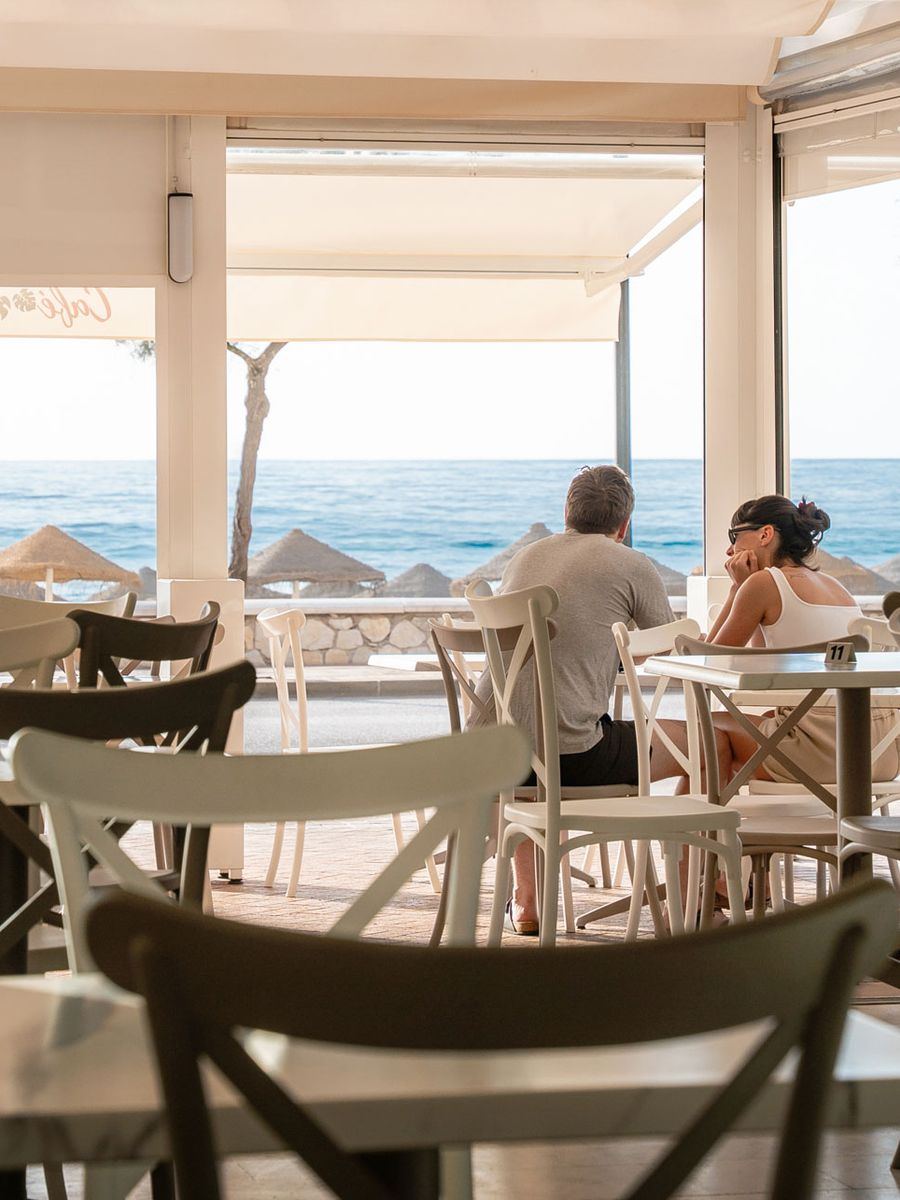 Blick vom Tisch: Strohschirme am Strand und dahinter das Mittelmeer.
